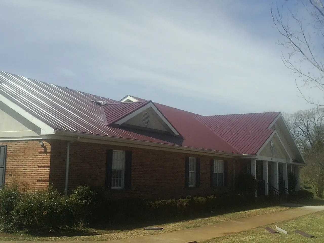 Red metal roof with gabled entries on a long brick building, from a Hail Damage Roof Repair job in Rising Fawn