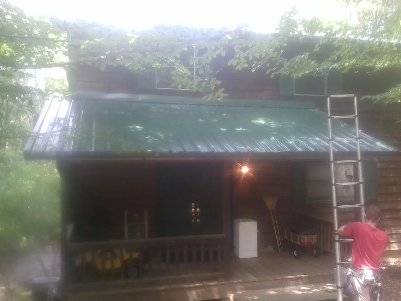 Worker on a ladder at the green porch roof of a wooded cabin in Rising Fawn