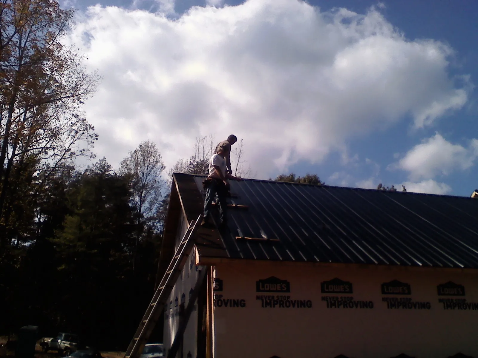 Roofer fastening dark metal panels high against a cloudy sky, from a Roof Inspection job in Rising Fawn