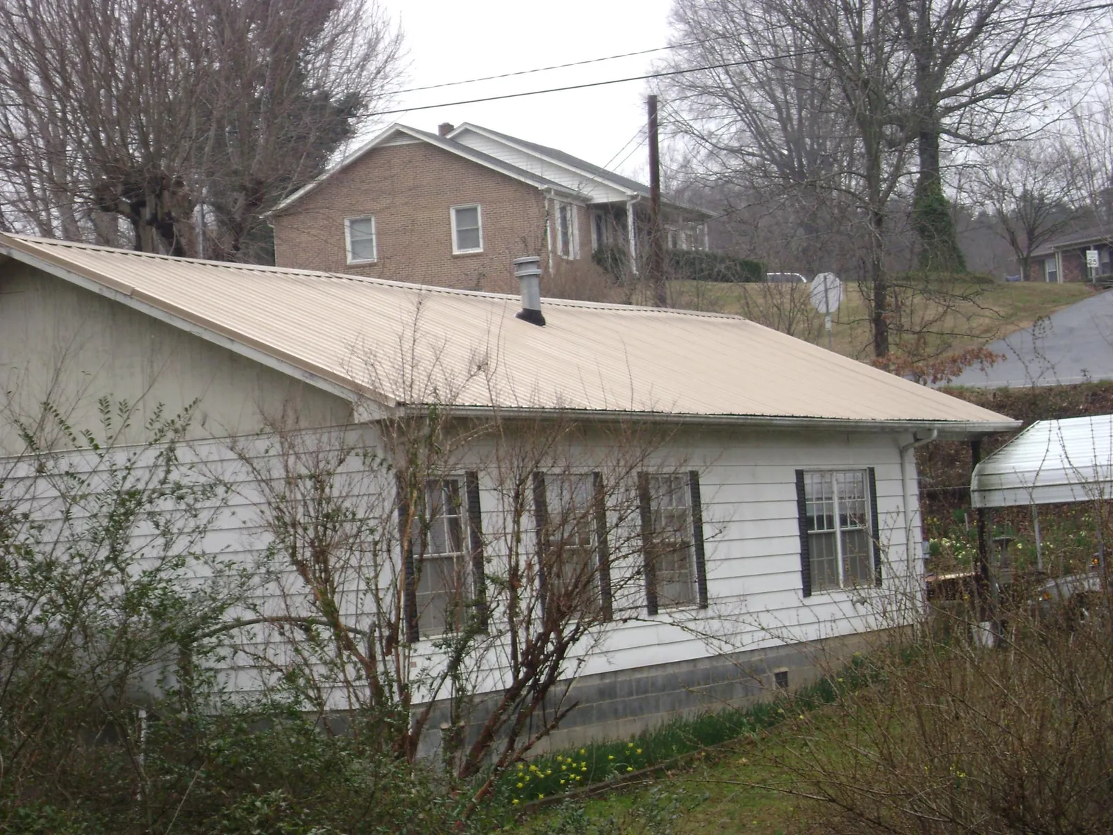Tan metal roof on a white sided house set into a hillside — Commercial Roofing by Roofing Brothers in Rising Fawn