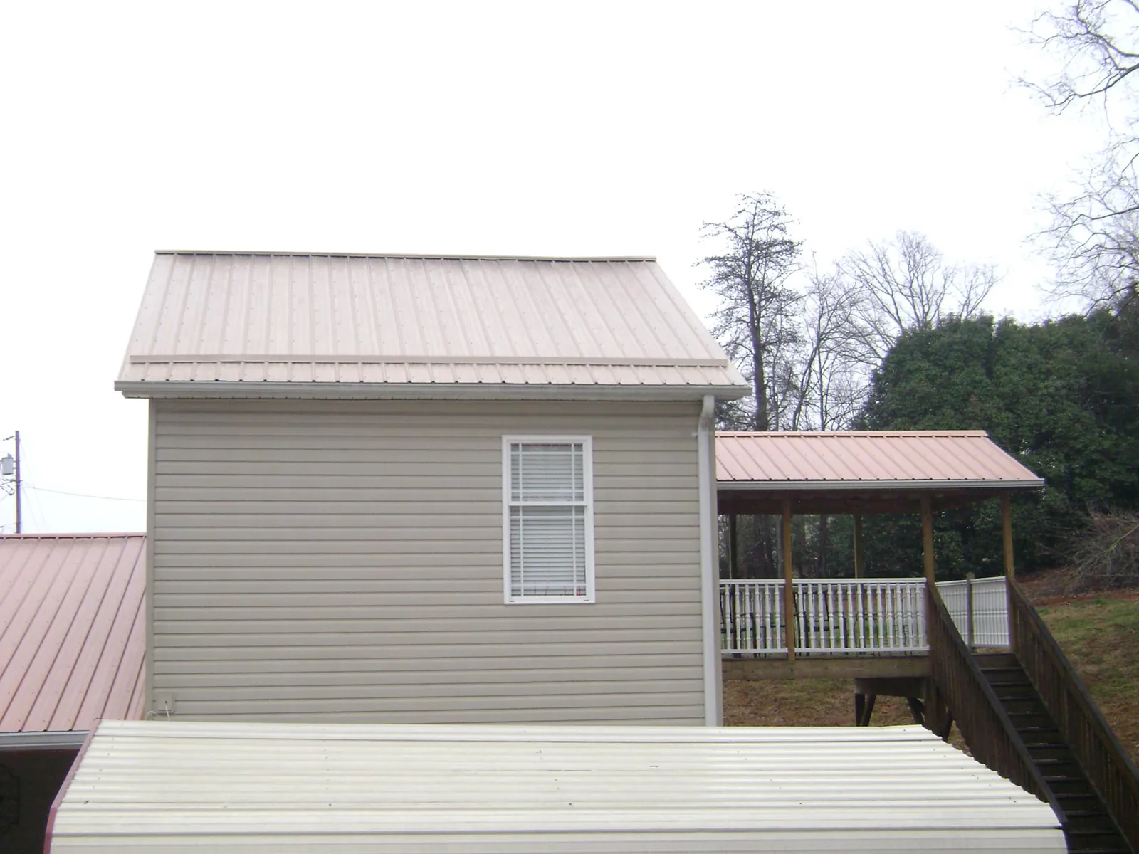 Tan metal roofs on a two story addition and attached porch, from a Roof Replacement job in Rising Fawn